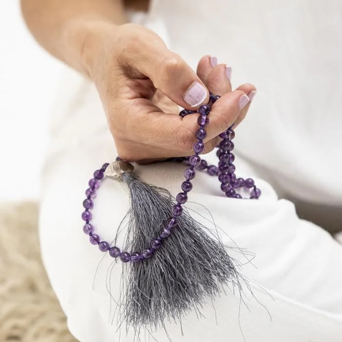 Manos de Luisa Convers sosteniendo una mala de amatista en meditacion
